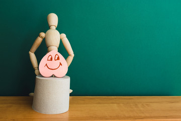 Wooden figure with a smiling heart sit on a roll of toilet paper. Concept of the problem with...