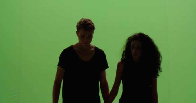 Distressed couple woman and man holding hands looking at each other in fear slow motion against green screen