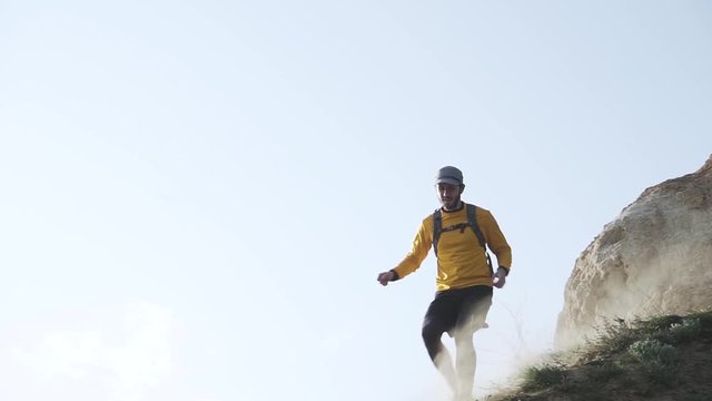 Young male trail runner with backpack training on the hill in sunny day 