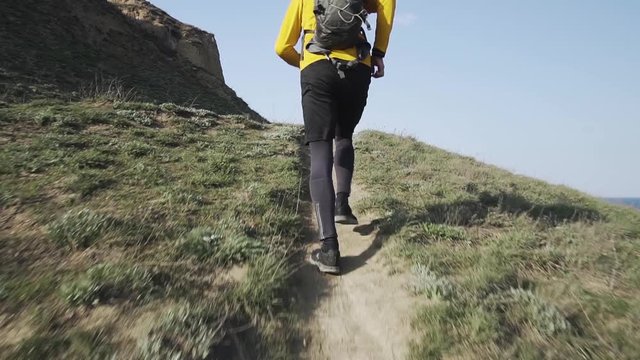 Young male trail runner with backpack training on the hill in sunny day 