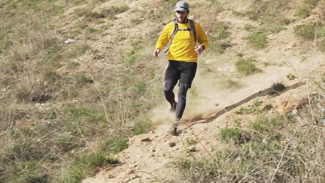 Young male trail runner with backpack training on the hill in sunny day 