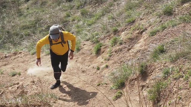 Young male trail runner with backpack training on the hill in sunny day 