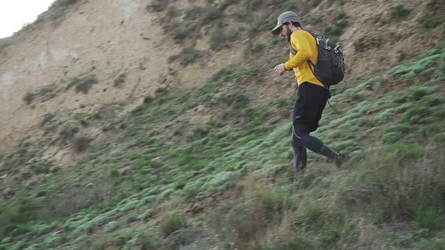 Young male trail runner with backpack training on the hill in sunny day 