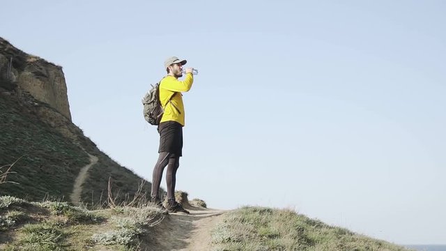Young male trail runner with backpack training on the hill in sunny day 