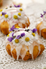 Obraz na płótnie Canvas Easter cakes covered with icing decorated with spring and edible flowers on lace white tablecloth, close-up. Easter delicious dessert