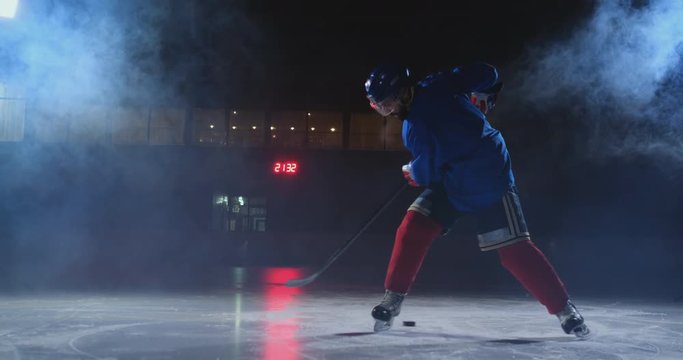 Professional hockey player with a stick and a puck moves on Luda in skates and helmet on a dark background and smoke. Dribbling with the puck of a young man on the ice arena