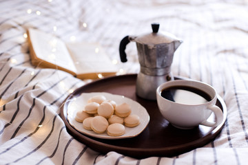 Cup of coffee with cookies on plate and open book at background in bed. Good morning. Tasty breakfast.