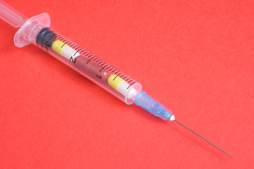 Fototapeta premium The concept of choice between treatment methods - pill or vaccine. Syringe with capsules on a red background.