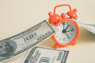 Concept time for financial gain. Red vintage clock with one hundred US dollar bills on a yellow background. Toned.