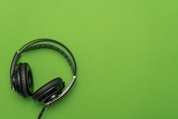 Black headphones for listening and mixing music on green background. Top view