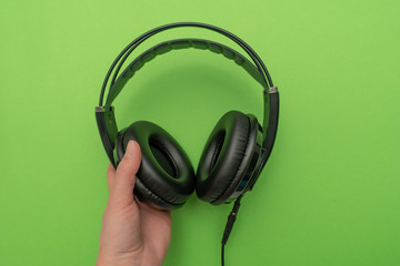 Fototapeta na wymiar Human's hand holding black headphones for listening and mixing music on green background. Top view