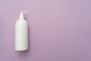White plastic bottle of liquid cosmetic(soap, shampoo, lotion) with a dispenser on the left on a purple background