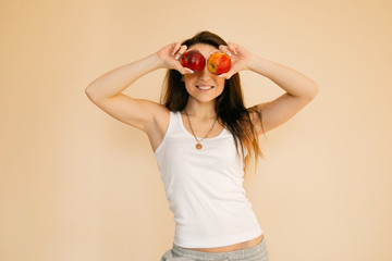  young woman in a white T-shirt chooses an apple, portraits on a uniform beige background