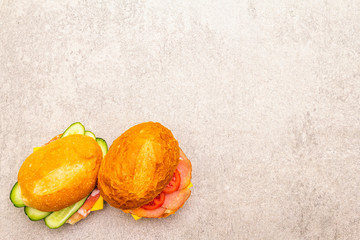 Homemade sandwich in bun. Salami, dried pork, tomato, cucumber, cheese ingredients. On stone background, top view.