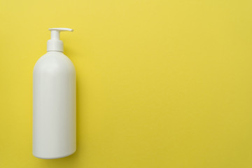 White plastic bottle of liquid cosmetic(soap, shampoo, lotion) with a dispenser on the left on a yellow background