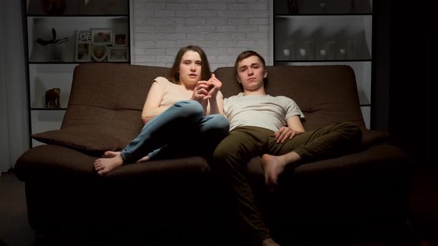 Young people watch a horror movie on TV and shudder in fear.