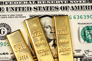 A close up image of an American one dollar bill with three small gold bars in macro