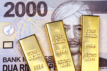 Three small gold bars with a 2000 Indonesian rupiah bank note close up in macro