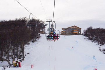 Naklejka premium Back view of a full moving lift in Castor ski center, on a cloudy winter day, with a big practice and racing slope below and a restaurant on the background, with copy space for text. Ushuaia Argentina