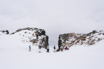 Center front view of a gap in the rocky mountains, with skiers talking and waiting on a ski slope, on a cold winter cloudy day. In Castor ski center, Ushuaia, Tierra del Fuego, Argentina.