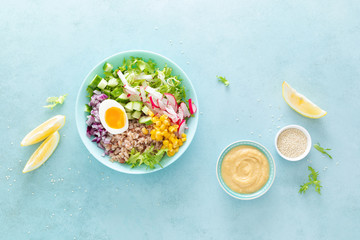 Buddha bowl with boiled egg, rice and vegetable salad of fresh lettuce, radish, cucumber, corn, onion and sesame seeds and chickpea sauce