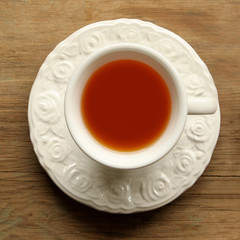 Tea in a white cup with a saucer and a spoon on a wooden table, square