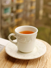 Tea in a white cup with a saucer stands on a light board on a background of greenery and houses