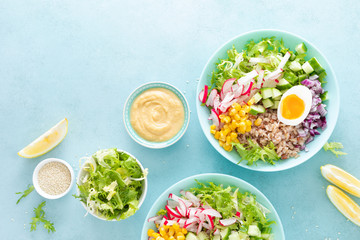 Buddha bowl with boiled egg, rice and vegetable salad of fresh lettuce, radish, cucumber, corn, onion and sesame seeds and chickpea sauce