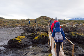Colorful dressed tourists walking on a bridge to a Patagonian Island in Beagle Channel on a tour excursion, on a cold winter cloudy day. Ushuaia,  Tierra del Fuego, Argentina.