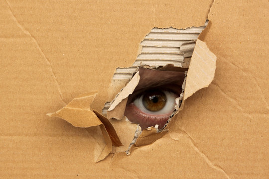 The human eye looks out of a hole in the cardboard, the concept of surveillance, peeping