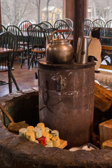 Detail of an interior old metal heater with a couple of kettles, many white and yellow mugs and some big firewood