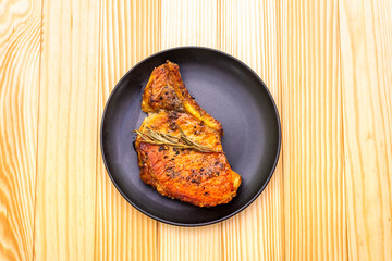 Cooked pork steak with spices and herbs. In a black plate on a wooden background, top view.