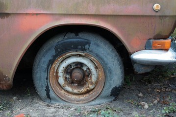 part of an old brown car with a gray flat tire on the sand