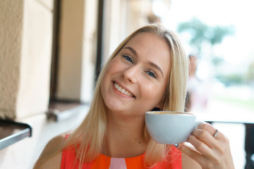 young beautiful blond woman sit at table in cafe drink coffee wait for businesspartner have a business meeting