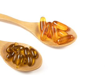 Fish oil capsules with omega 3 and vitamin D in a wooden spoon on white background, healthy diet...