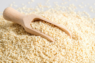 Close up. A wooden spoon filled with seeds lies on a pile of sesame. White background.