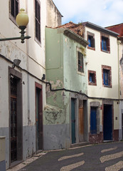 a typical quiet empty street in funchal madeira with old traditional houses painted in faded pastel...