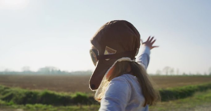 Authentic shot of cute little girl with aviator hat having fun and smiling in camera on a spring nature background in a  sunny day.