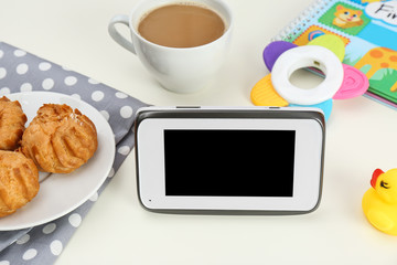 Modern monitor, cup of coffee, cookies and baby accessories on table, space for text. CCTV equipment