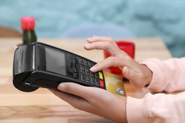 Woman using card machine for non cash payment at table, closeup