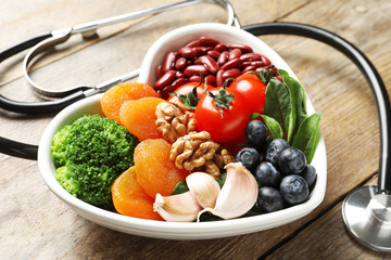 Bowl with products for heart-healthy diet and stethoscope on wooden table