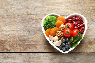 Bowl with heart-healthy diet products on wooden background, top view. Space for text