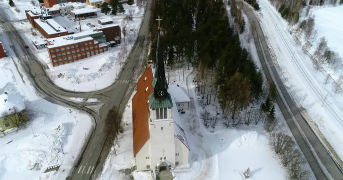 Lapland town, C4k aerial, tilt up, drone shot, away from Kemijarvi church, revealing a the village, road e63 and wilderness, on a cloudy, winter day, at the arctic circle, in Lapland, Finland