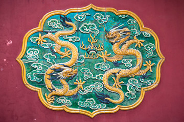 Two dragons Glazed Tiled on a Red Wall in beijing. Dragons are important in Buddhist art and myths