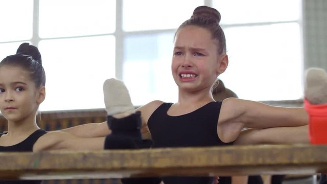 Sequence of videos of teenage girls in bodysuits using chairs to do stretching exercises and practicing splits in dance class