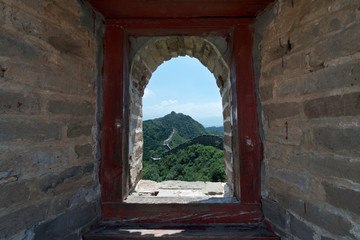 View through a brick window of a Fortress Guard Tower of Mutianyu, a section of the Great Wall of China during summer. Huairou District, Beijing, China