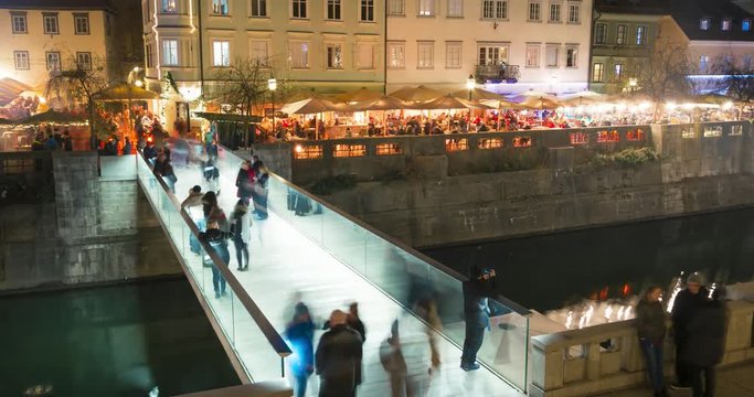 Nightime Ljubljana city timelapse of a small bridge with people walking over it on new years eve. More people can be seen in the caffee near the water wall.
