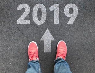 top view of feet , white arrow and 2019 text on asphalt road , start new year concept