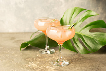 Refreshing summer cocktail of grapefruit juice and ice glass goblets a gray concrete background with leaves of Monstera.