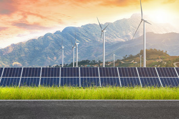 Asphalt road with solar panels with wind turbines against mountanis landscape against sunset...